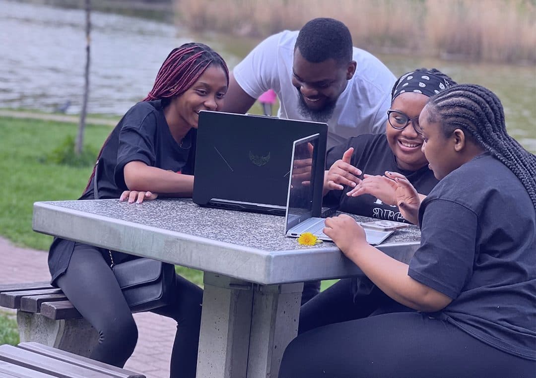 Four members of the DigitalGeeks team working together around a laptop at an outdoor table